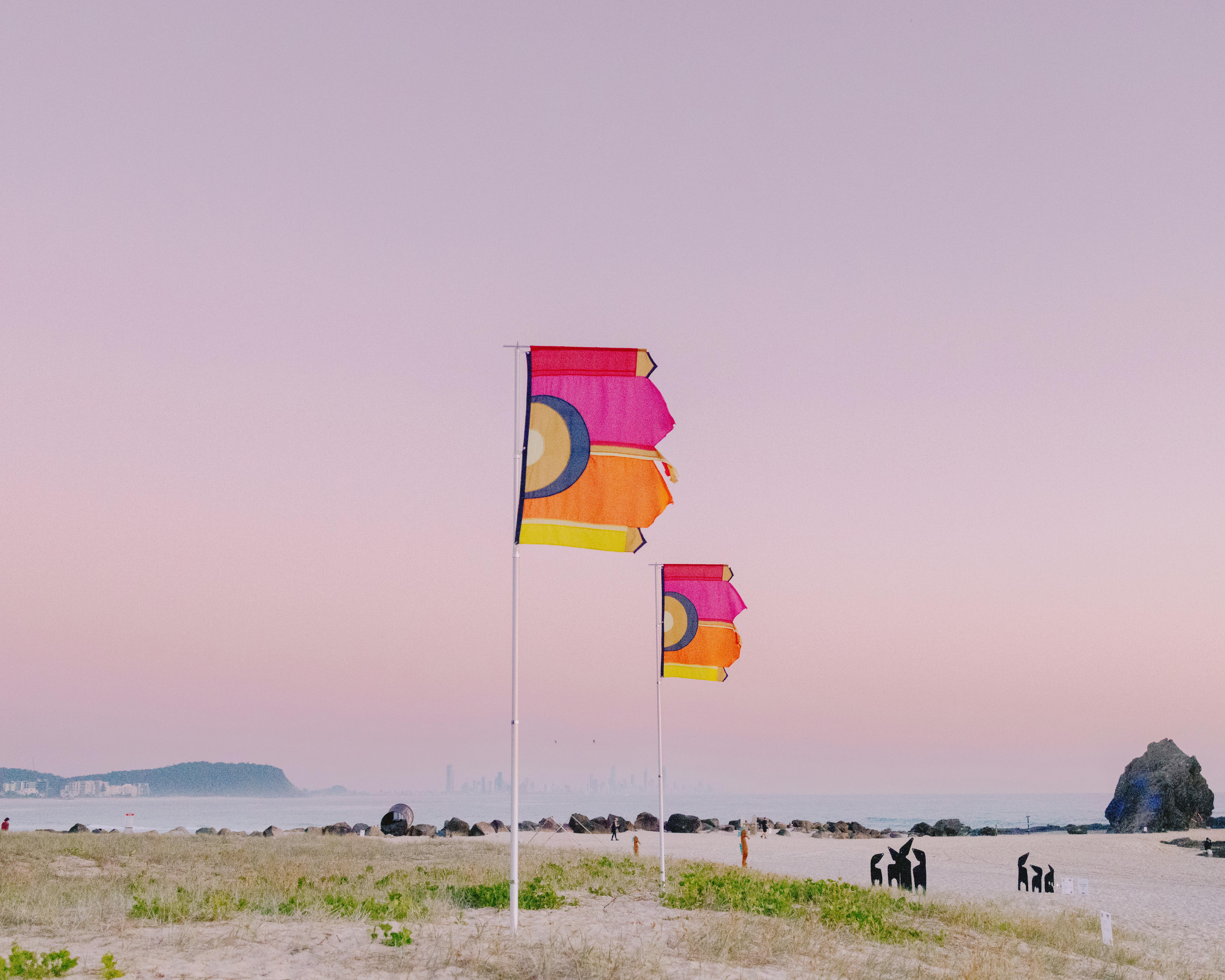 Colorful flags waving on Currumbin Beach with a stunning pink sunset sky, capturing the serene coastal scene.