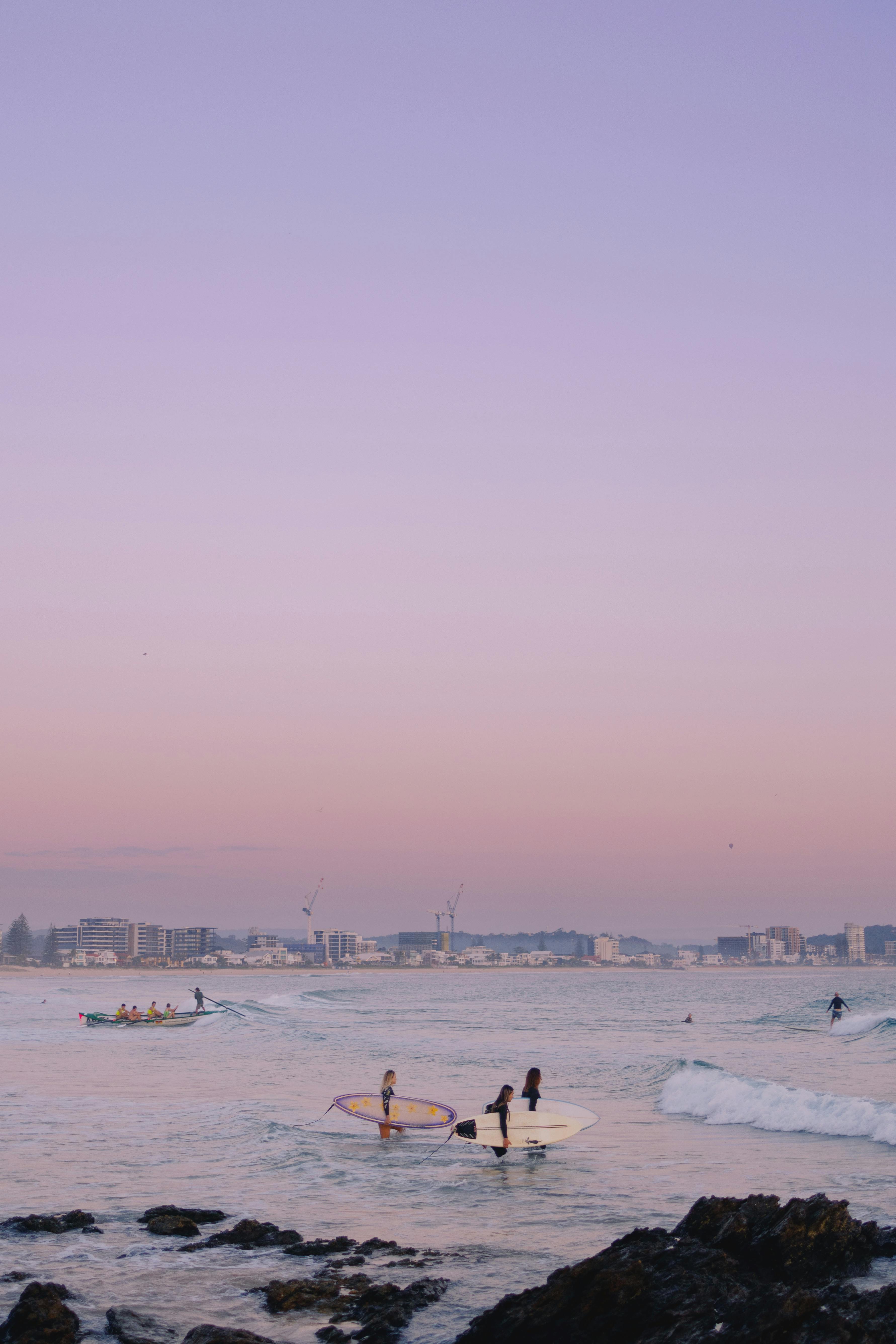 Surfers enjoy the waves at Currumbin Beach, Australia during a beautiful pink sunset.