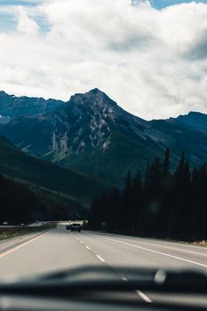 Beautiful highway view of mountains in Jasper, Alberta with cars and trees.