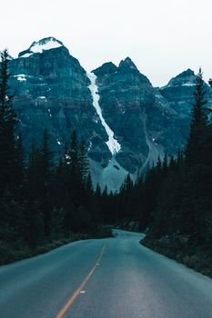 Dramatic view of snow-capped mountains along a forest road in Banff, Canada.