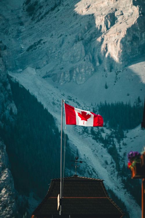 Free Canadian flag flying against the backdrop of Banff's rocky mountain landscape. Stock Photo