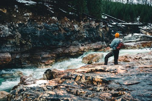 Free A lone hiker stands by a rushing river in Kootenay Crossing, embracing the wilderness. Stock Photo