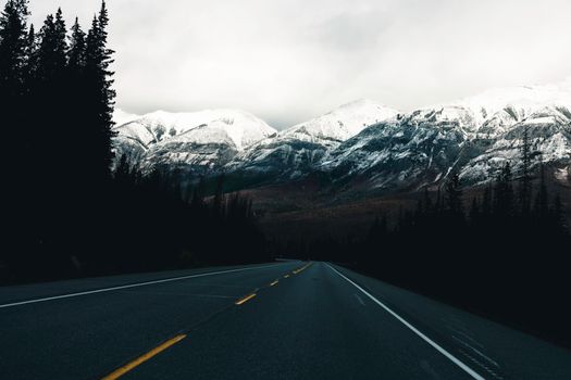 A breathtaking view of a road leading into the snow-capped mountains in Kootenay Crossing, BC, Canada.