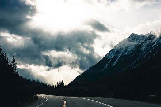 Scenic view of a highway winding through Kootenay Crossing, BC, with mountains under dramatic clouds.