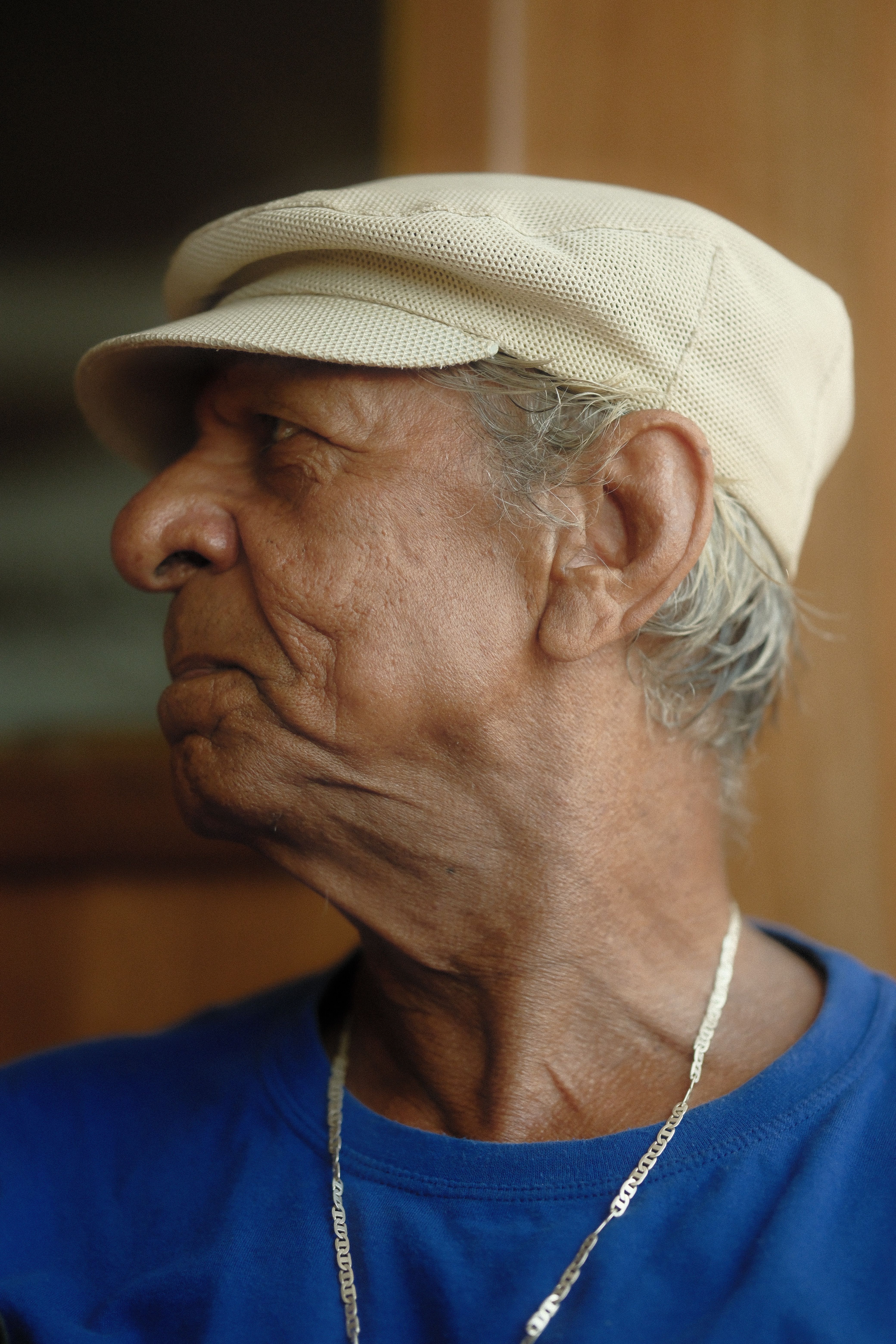 Close-up profile portrait of a senior man wearing a cap and chain.