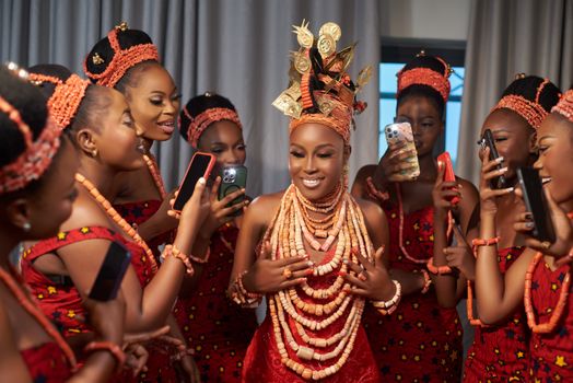 Group of African women in traditional red attire, elegantly posing and smiling with smartphones.