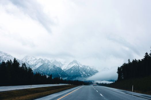 A foggy highway surrounded by snowy mountains in Glacier National Park, Canada.