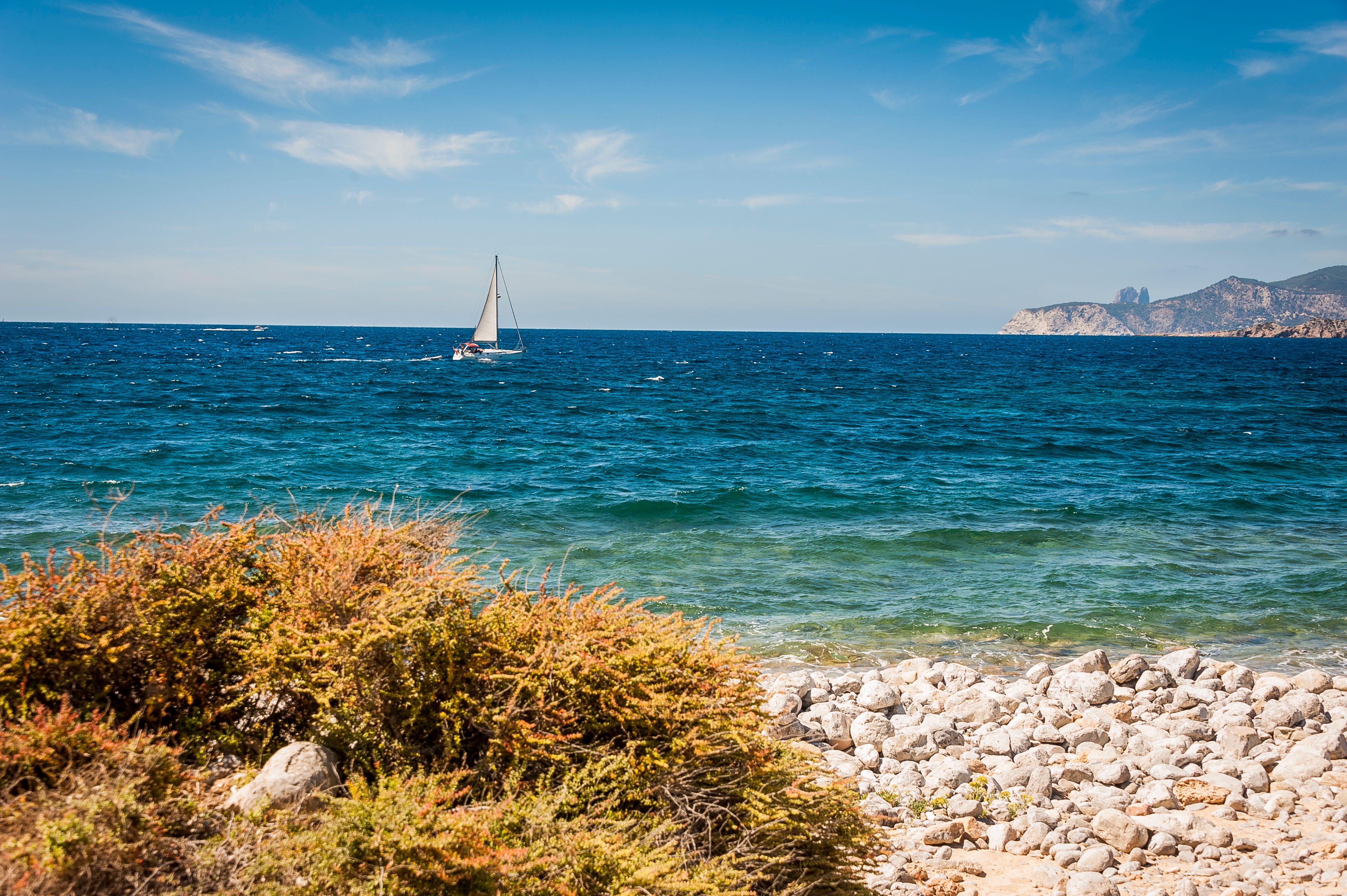 Unbeatable 2 Hour Shared Sailing Tour in Barcelona with Open Bar & Snacks Review: Justin's Complete Guide Review 2026 - A tranquil scene of a sailboat on the deep blue ocean with a rocky shoreline in the foreground.