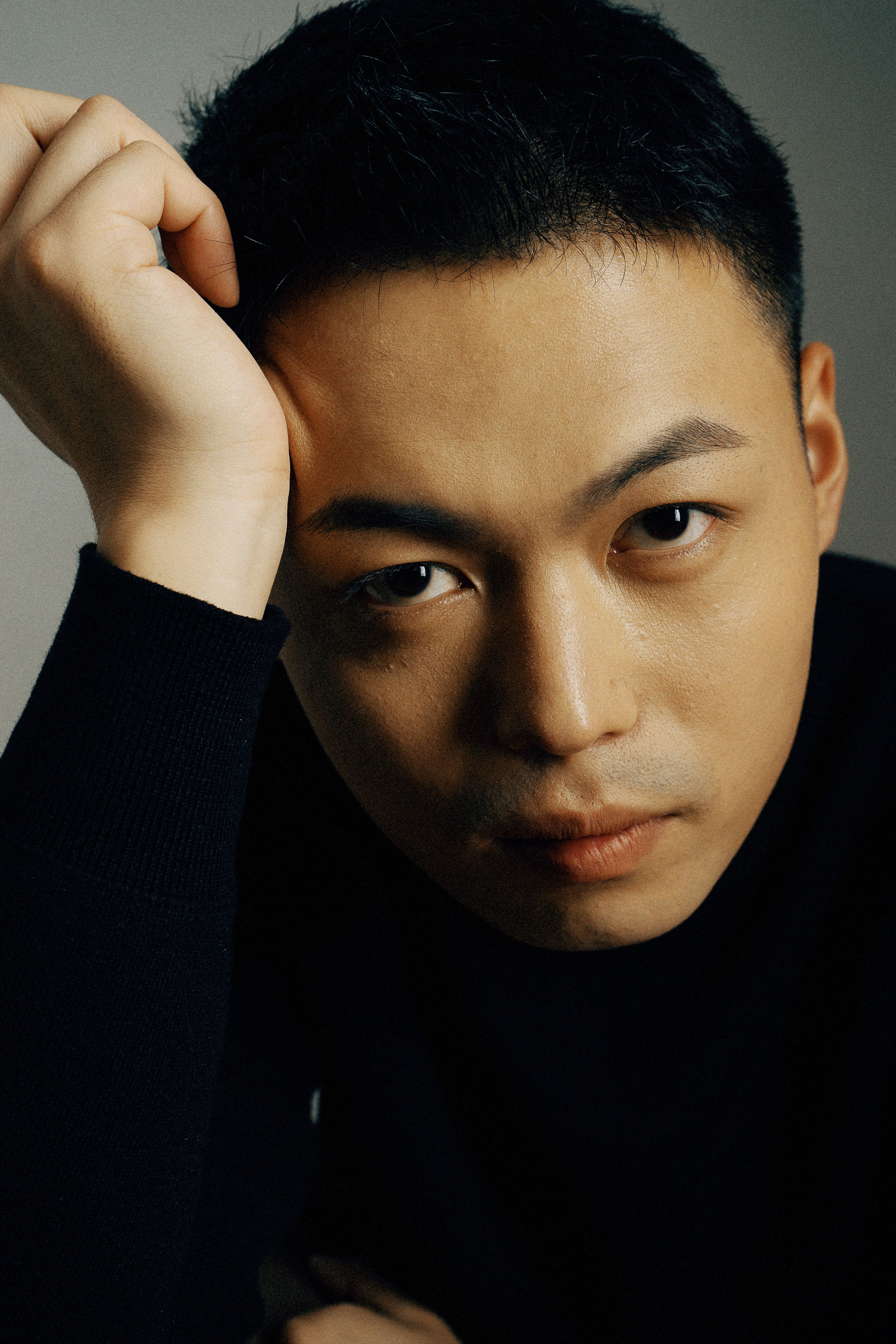 A dramatic portrait of a young Asian man in a studio setting, exuding a serious expression.