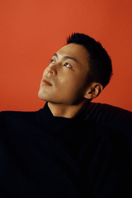 Stylish portrait of a man looking thoughtfully upwards against a bold red background.