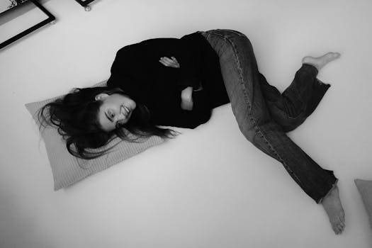 Black and white image of a woman lying on a bed, casually dressed in jeans.