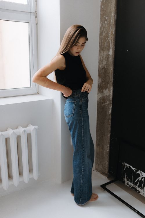 Woman in black top and barrel jeans by a window