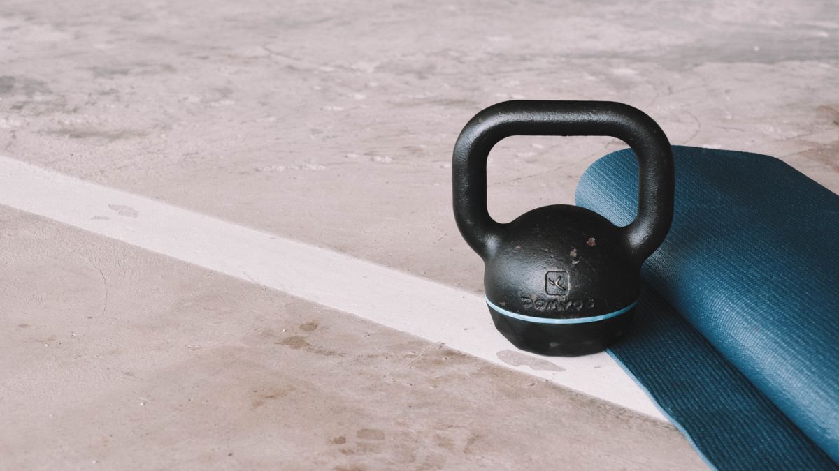 Kettlebell and blue yoga mat on a concrete floor in an indoor gym setting.