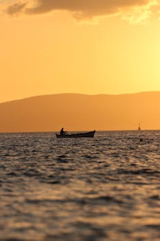 Silhouetted fisherman on a boat during a golden sunset in Naxos, Greece. Tranquil and picturesque.