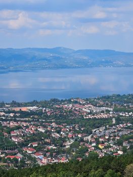 Scenic aerial view of a lakeside town with distant mountains under a clear sky.