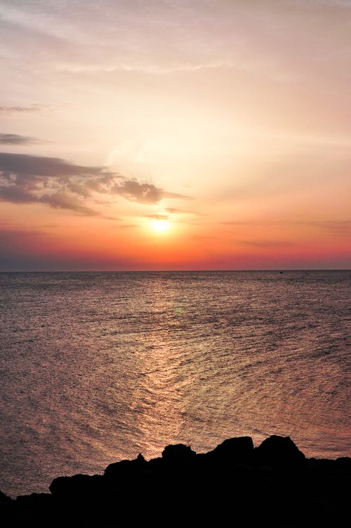 Free Tranquil sunset over a calm ocean with a rocky shoreline, perfect for relaxation themes. Stock Photo