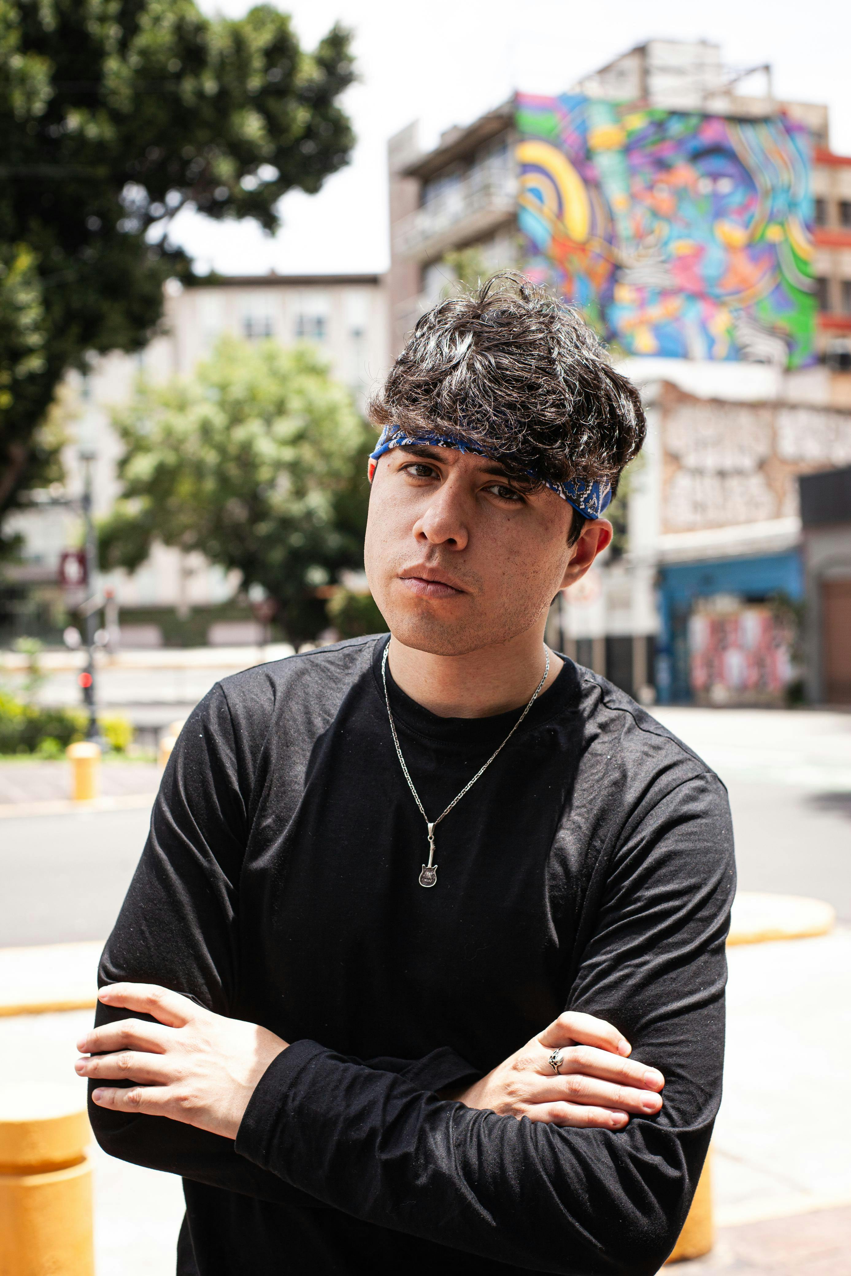 Young man with crossed arms poses in front of vibrant street art in an urban setting.