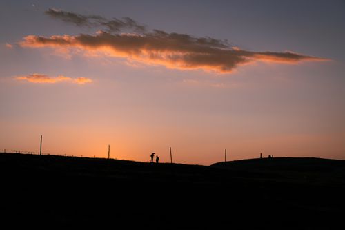 Free Silhouettes stand against a vibrant sunrise in a serene mountain setting. Stock Photo