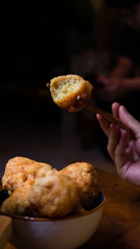 A close-up of delicious homemade fried meatballs being picked up with chopsticks from a bowl.
