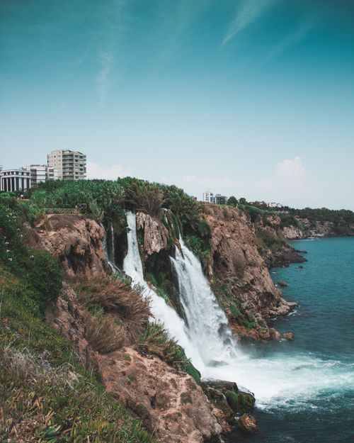Free A stunning view of a waterfall flowing over cliffs into the sea with clear skies above, offering tranquility. Stock Photo