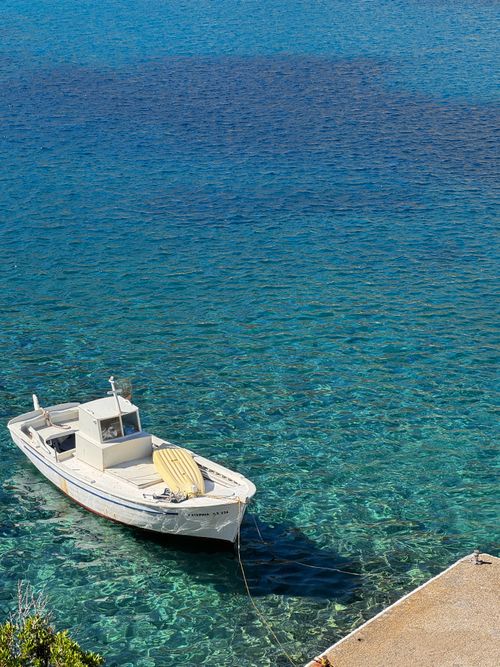 Free A peaceful scene of a fishing boat moored in the crystal clear waters of a Greek island. Stock Photo