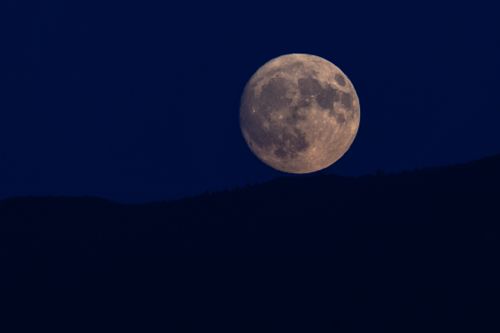 Free A breathtaking view of a full moon rising over a dark hill silhouette against a deep blue night sky. Stock Photo