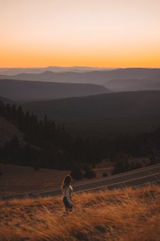 一名妇女站在草山上，俯瞰着夕阳西下的山谷和远处的群山