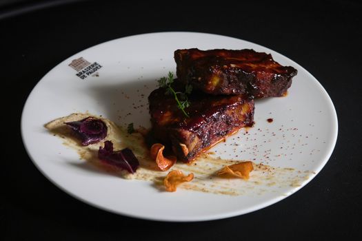 Delicious barbecue ribs with garnish on a white plate, perfect for gourmet food enthusiasts.