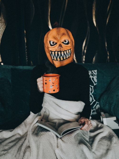 Free Person in pumpkin mask holding an orange cup, cozy Halloween theme indoors. Stock Photo