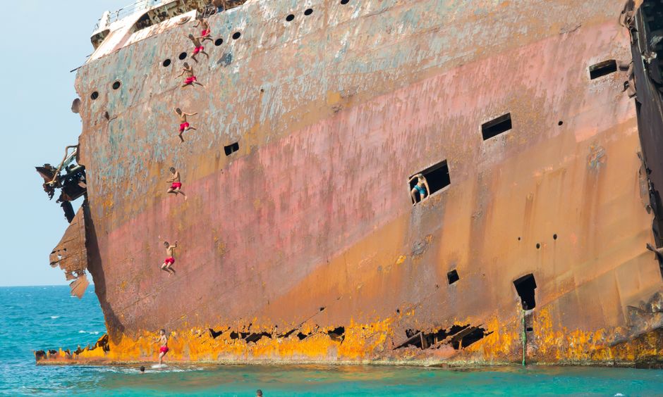 Adventurous individuals climbing a rusted shipwreck remains in Bizerte, Tunisia's clear waters.