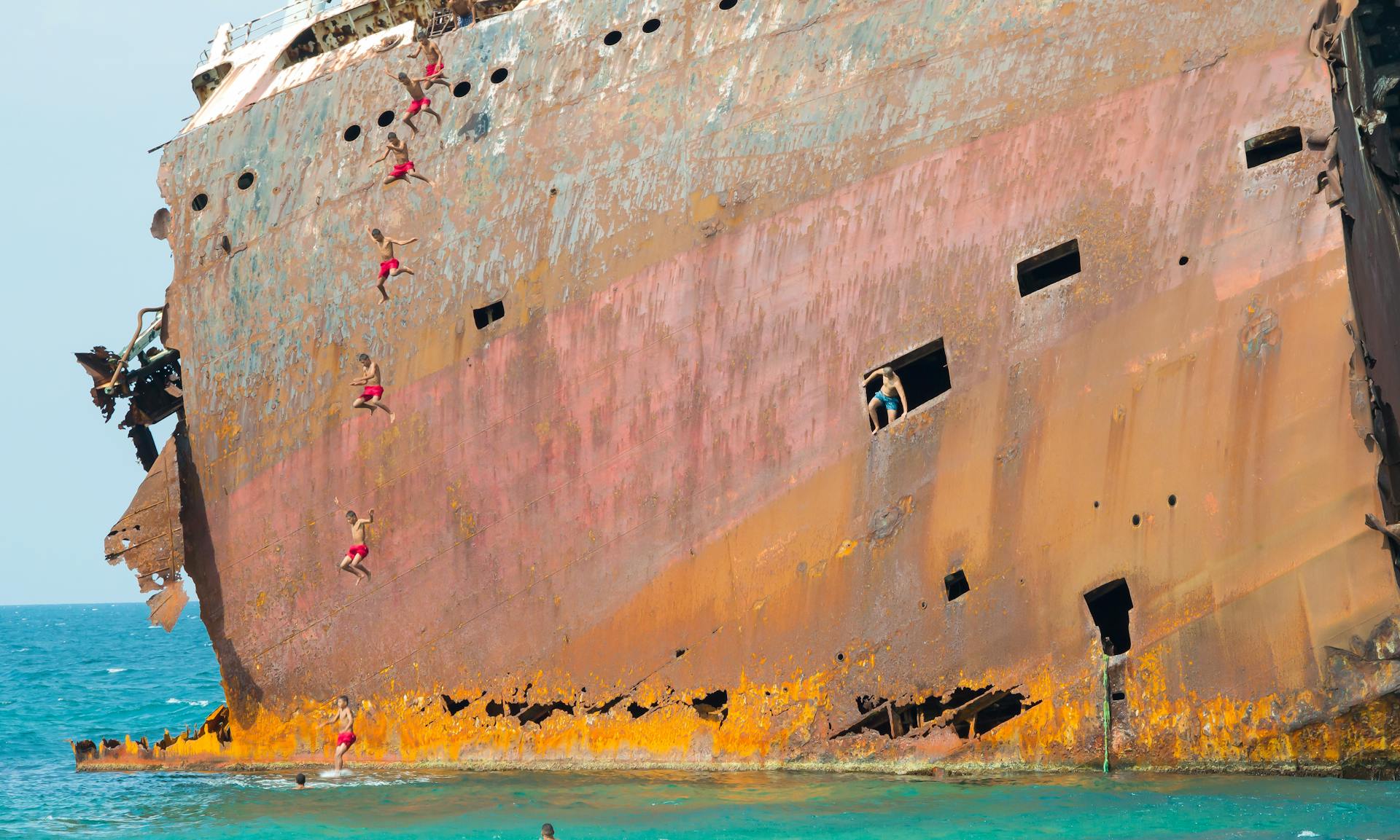 Adventurous individuals climbing a rusted shipwreck remains in Bizerte, Tunisia's clear waters.