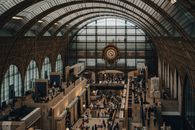 A bustling gallery inside Musée d'Orsay featuring a historic clock and crowds of visitors.