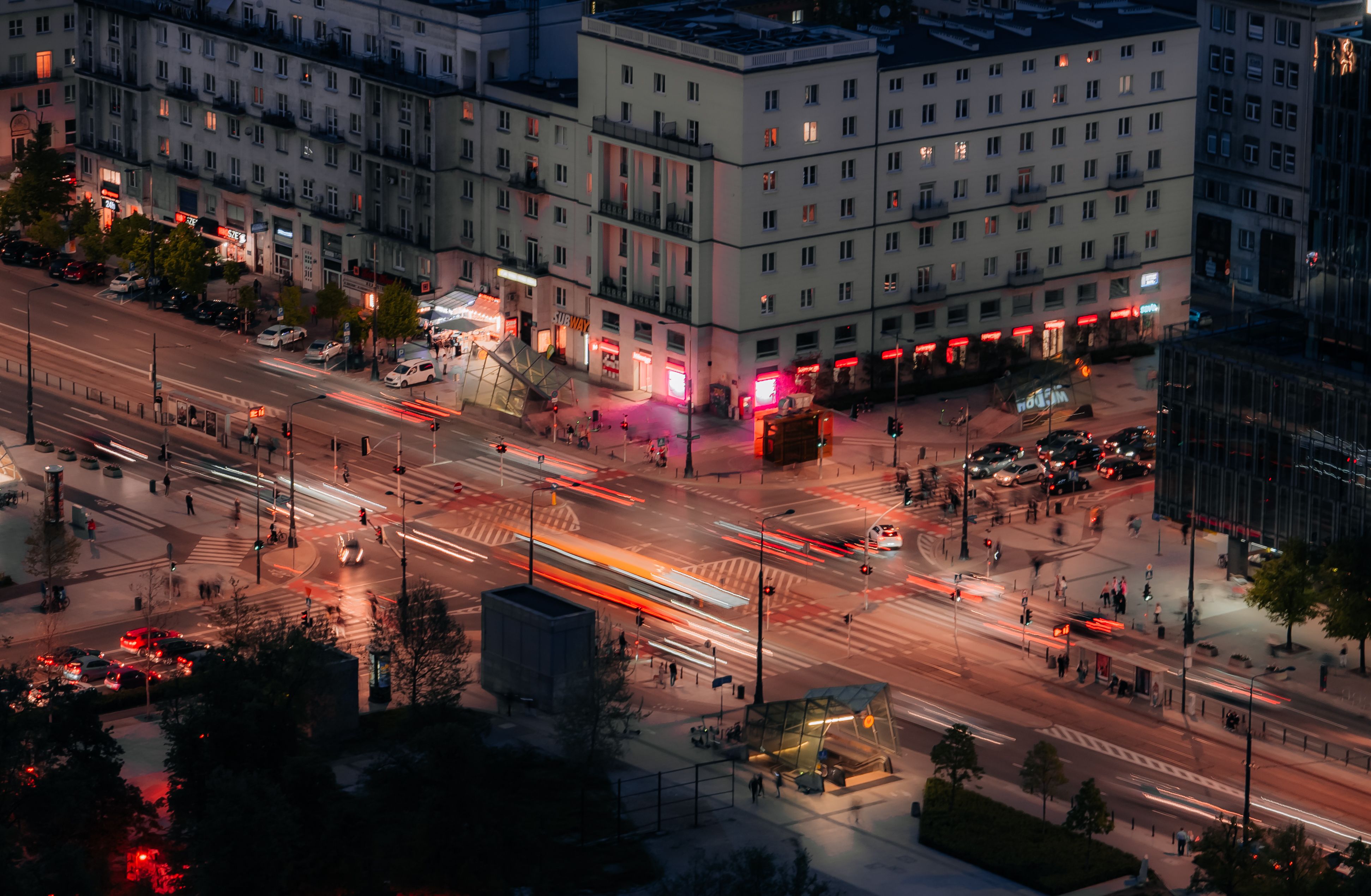Aerial nighttime view of a Warsaw intersection with traffic lights and buildings.