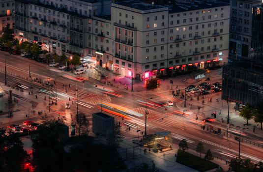 A bustling nighttime aerial view of a city intersection in Warsaw, featuring vibrant traffic lights and urban architecture.