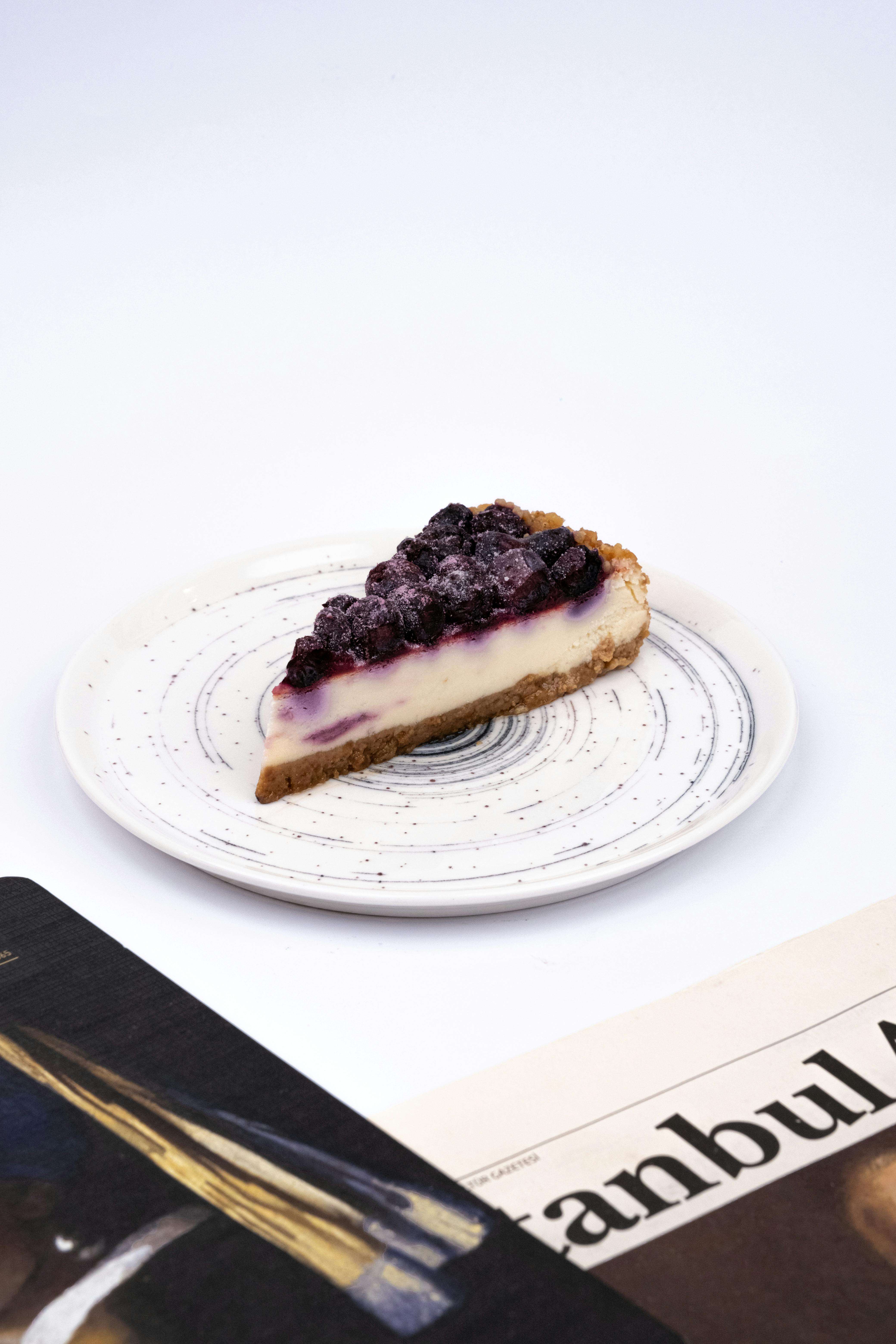 A delicious blueberry cheesecake slice sits on a stylish plate with a magazine nearby.