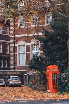 Quintessential London street view featuring a red phone booth and autumn leaves.