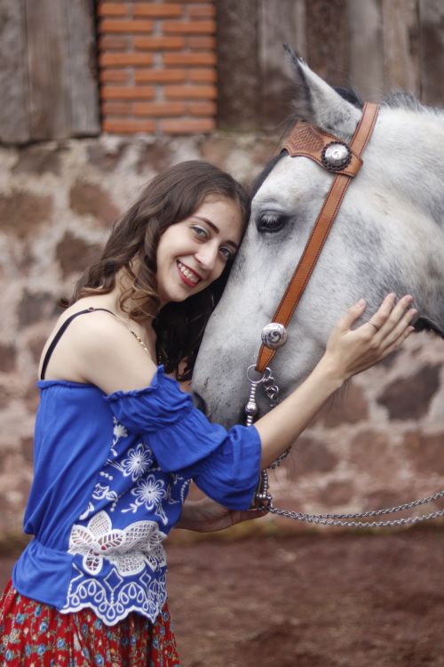 Free A smiling woman in a blue dress lovingly embraces a white horse outdoors. Stock Photo