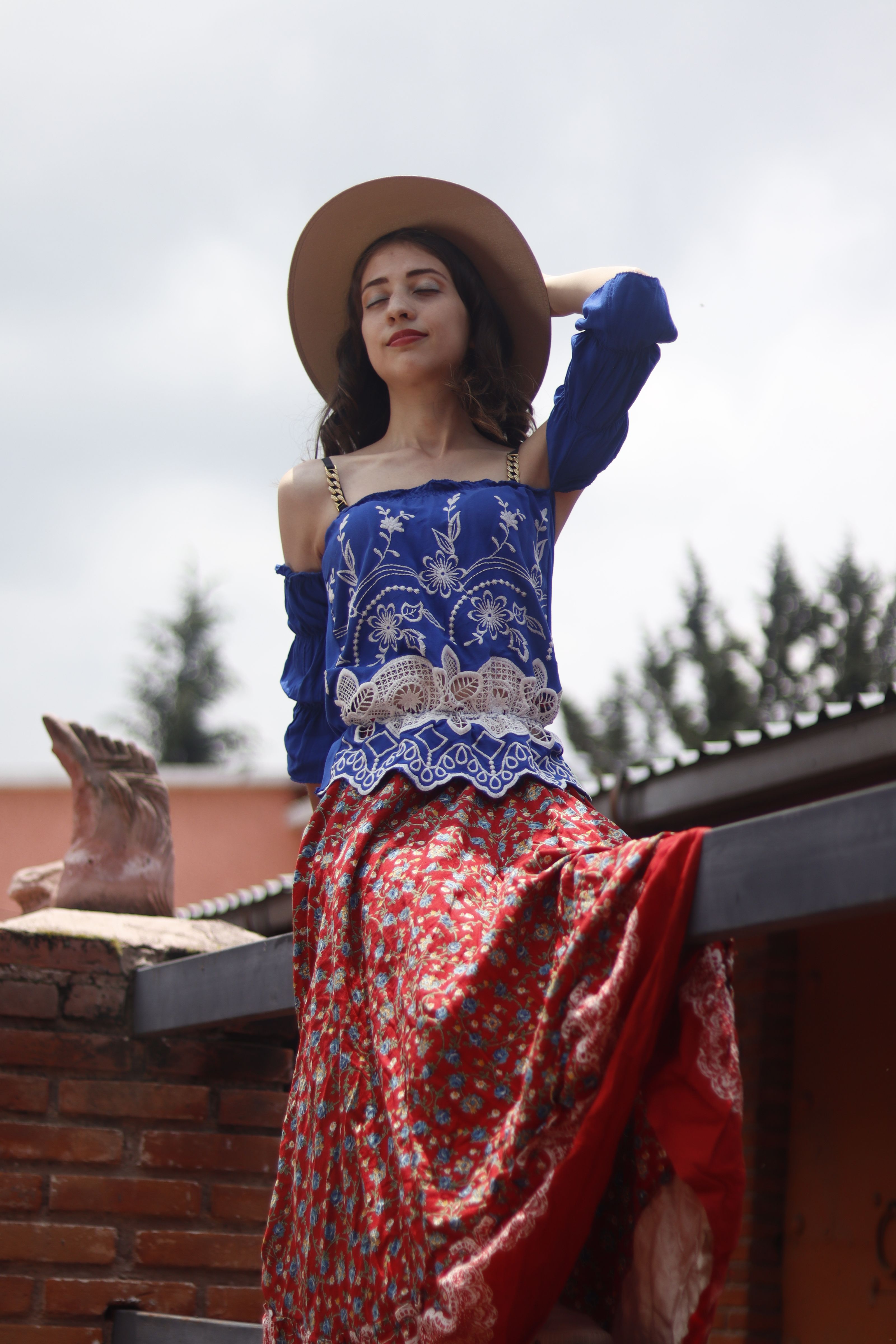 Mulher com traje boêmio posa ao ar livre com fundo rústico.