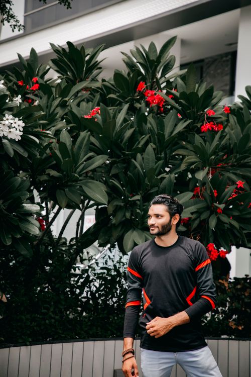 Free Portrait of a stylish man posing in front of lush greenery and red flowers. Stock Photo