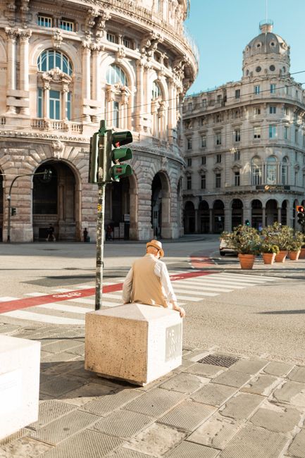 An elderly man sits in Piazza De Ferrari, showcasing Genova's historic architecture.