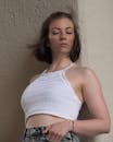 A woman in a white crop top leaning against a wall