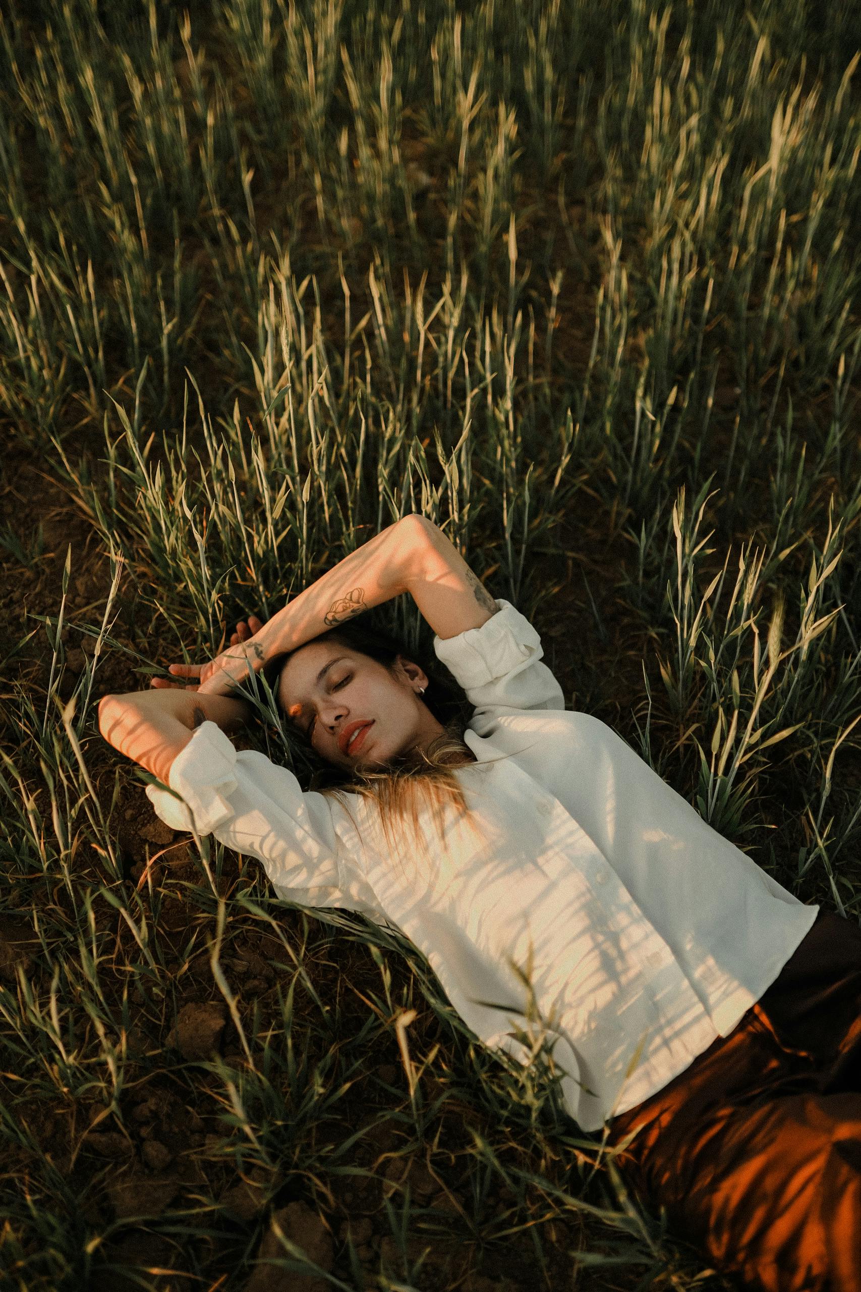 A woman in white shirt relaxing on grassy field under warm sunlight.