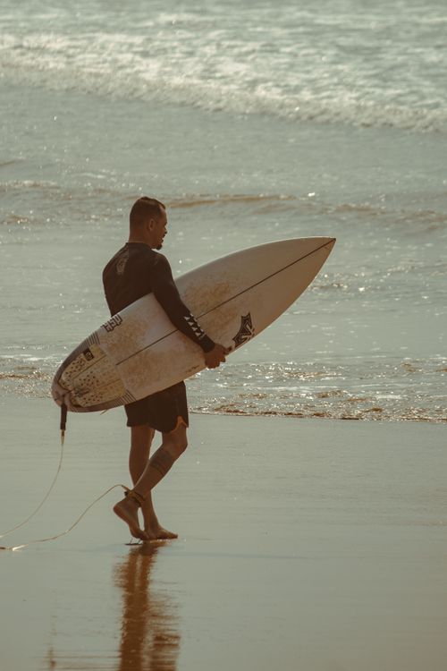 Free A surfer walking along a sunny beach with a surfboard, embracing the surf culture vibe. Stock Photo