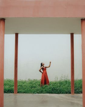 Stylish African woman in a vibrant red dress striking a pose amidst columns in Ibadan, Nigeria.