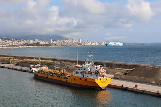 A vibrant yellow cargo ship docked in a bustling coastal port with cityscape background.