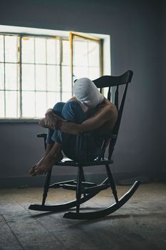 一个裹着布的人坐在黑暗房间的窗边木制摇椅上