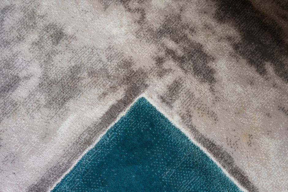 Close-up of a modern geometric carpet texture with teal and gray hues.