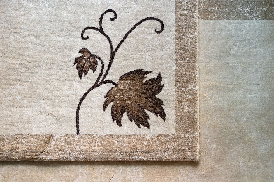 Close-up of an intricate leaf pattern on a textured beige fabric background, showcasing artistic design.