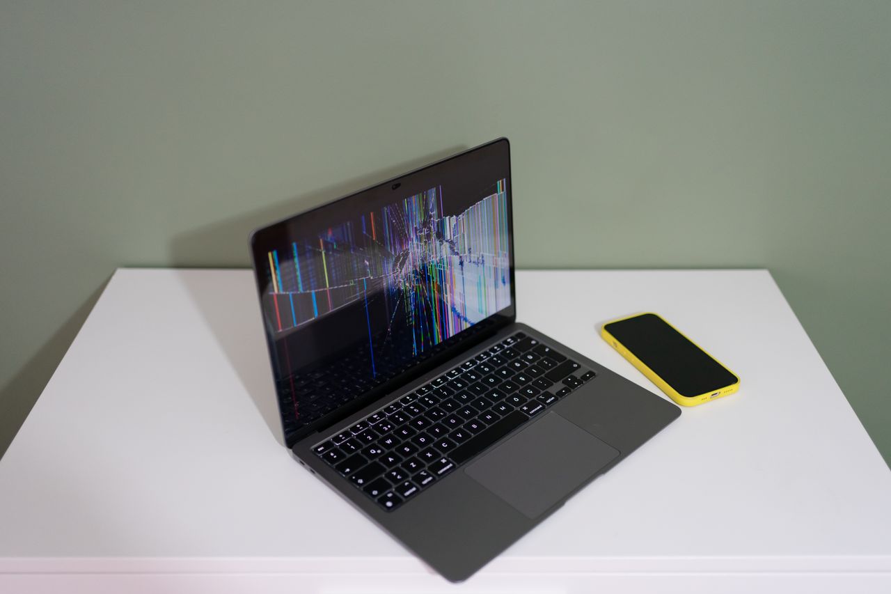 a damaged laptop screen with colorful lines and a yellow smartphone on