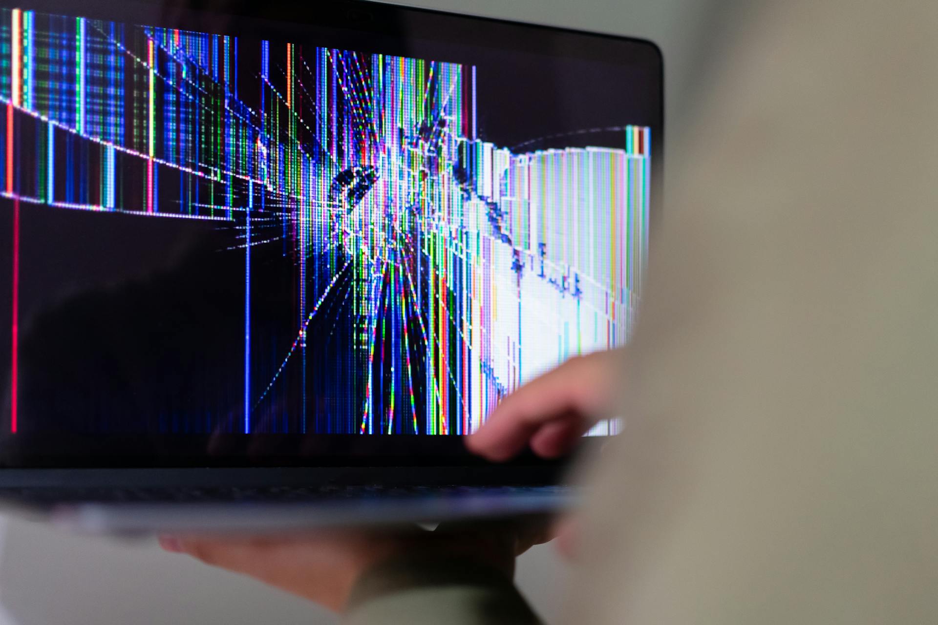 A person holding a laptop with a broken screen